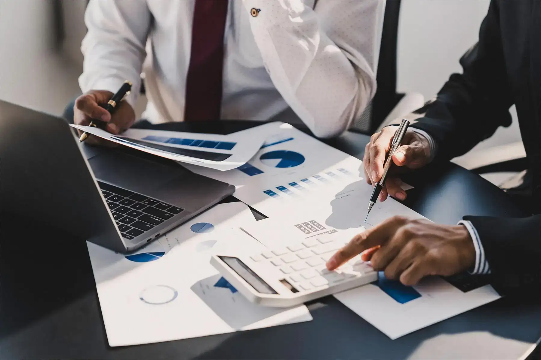 Due professionisti analizzano grafici e dati finanziari con laptop e calcolatrice su una scrivania