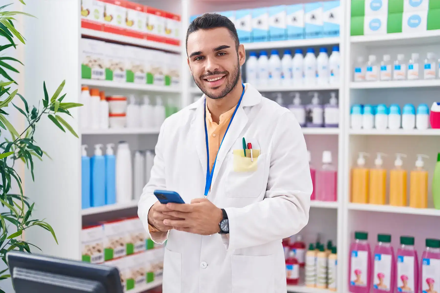 Un farmacista sorridente in camice bianco con uno smartphone in mano all'interno di una farmacia
